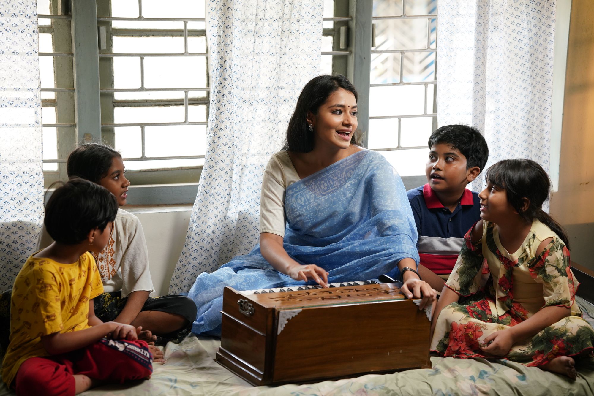 A teacher playing a harmonium while leading a music lesson with a group of children