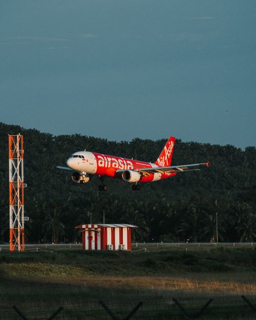 Free AirAsia Airbus A320 landing with tropical forest background, showcasing aviation travel. Stock Photo