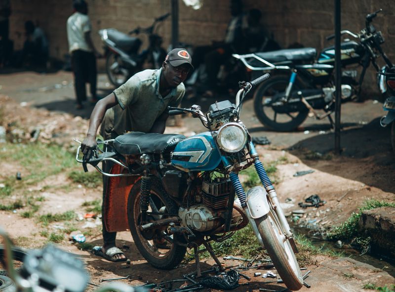 Mechanic repairing a motorcycle outdoors in Kaduna, Nigeria, showcasing local community craftsmanship.
