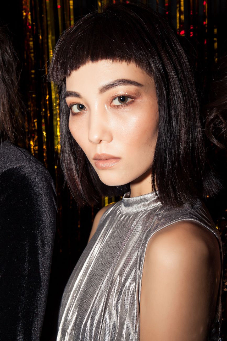 Stylish portrait of an Asian woman in silver dress, exuding elegance at a vibrant club setting.