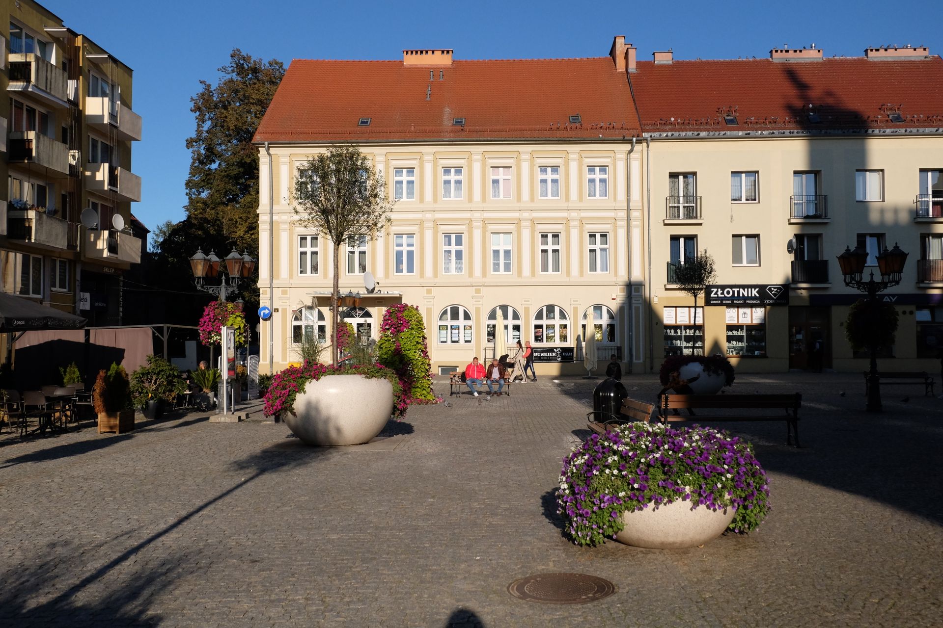 Picturesque European town square with colorful flowers and classic architecture in the afternoon sun.
