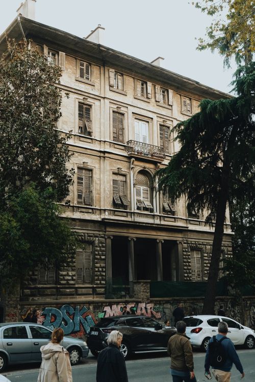 Free A vintage urban scene with pedestrians and graffiti on a historic building exterior. Stock Photo