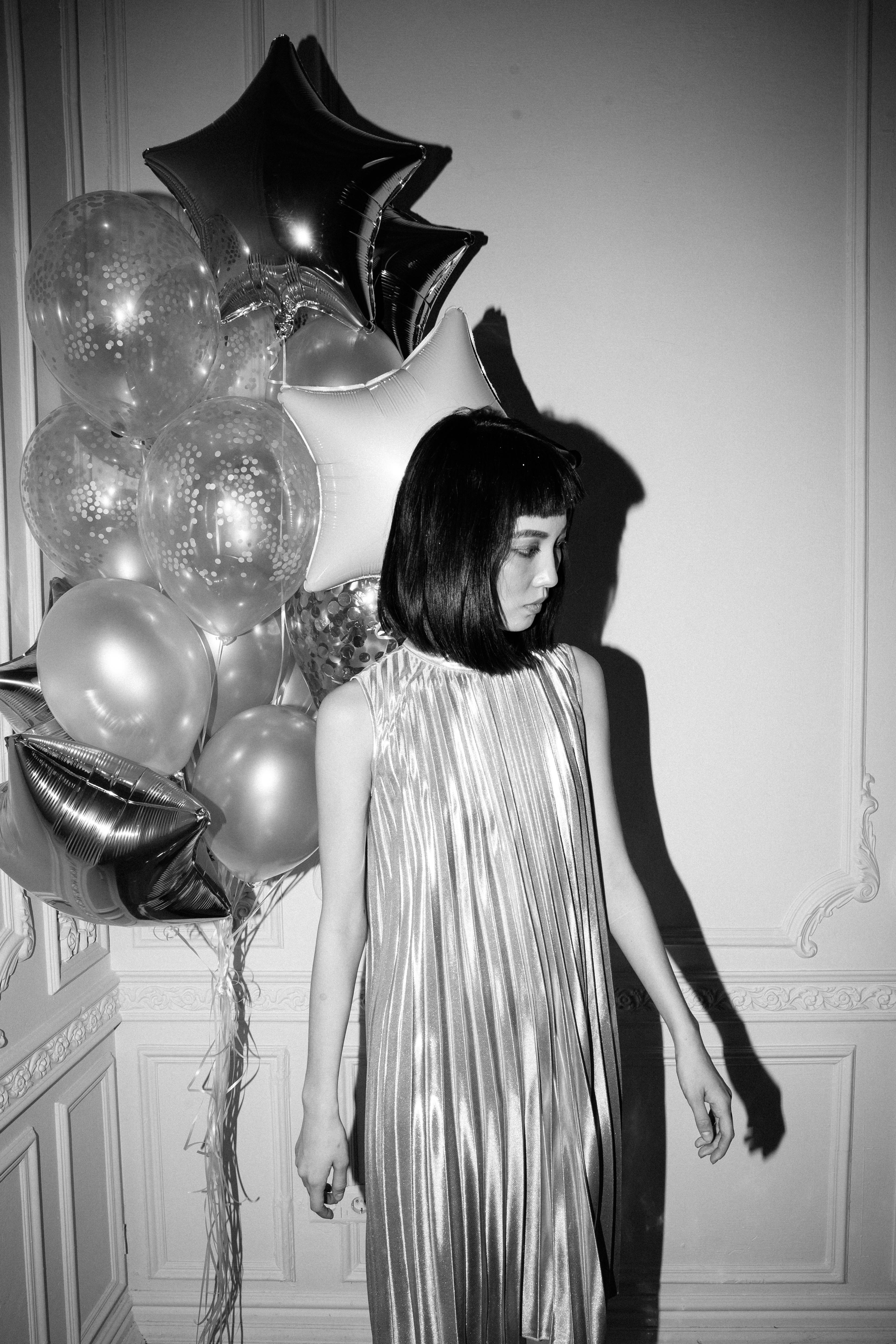 在黑白主题的派对上，一位身着褶皱连衣裙的时尚女士站在气球旁