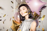 一位面带微笑的女性在节日氛围中，手持五颜六色的气球和五彩纸屑