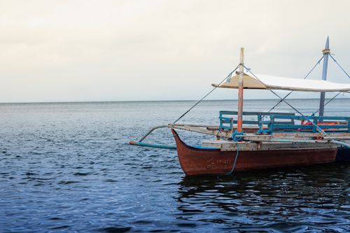 Free A classic wooden boat with a white canopy rests on a serene sea, perfect for coastal adventures. Stock Photo