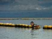 在戏剧性的天空下，一名青少年躺在海洋中的浮标上休息，形成了令人信服的对比