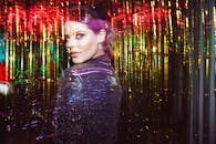 一位年轻女子在充满活力、色彩缤纷的环境中摆出姿势，闪闪发光的彩带营造出动态而时尚的外观