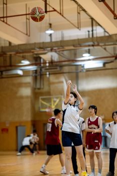 Teenagers playing basketball indoors, focusing on a player shooting a hoop.