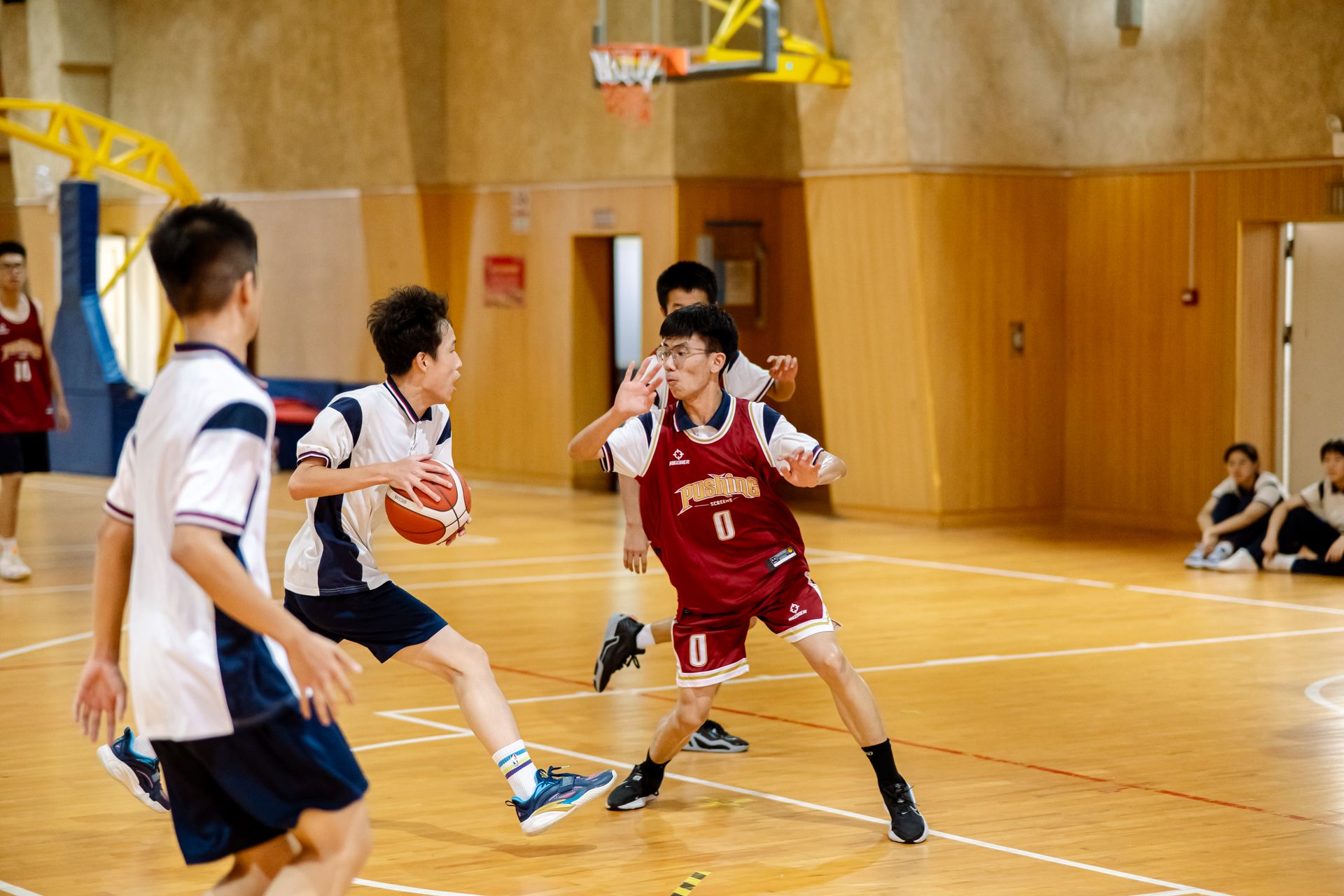 Dynamic action shot of teenagers playing basketball in a well-lit indoor court.