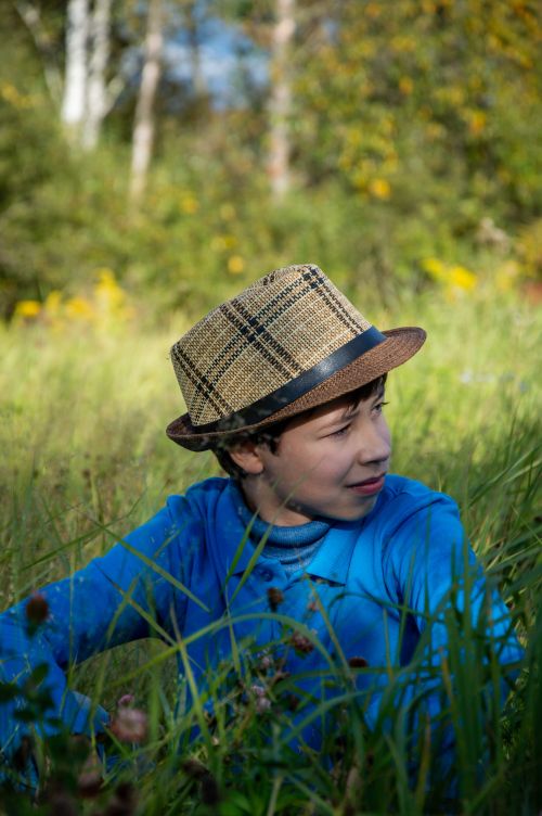Free A boy in a straw hat enjoys a sunny day outdoors, surrounded by lush grass and wildflowers. Stock Photo