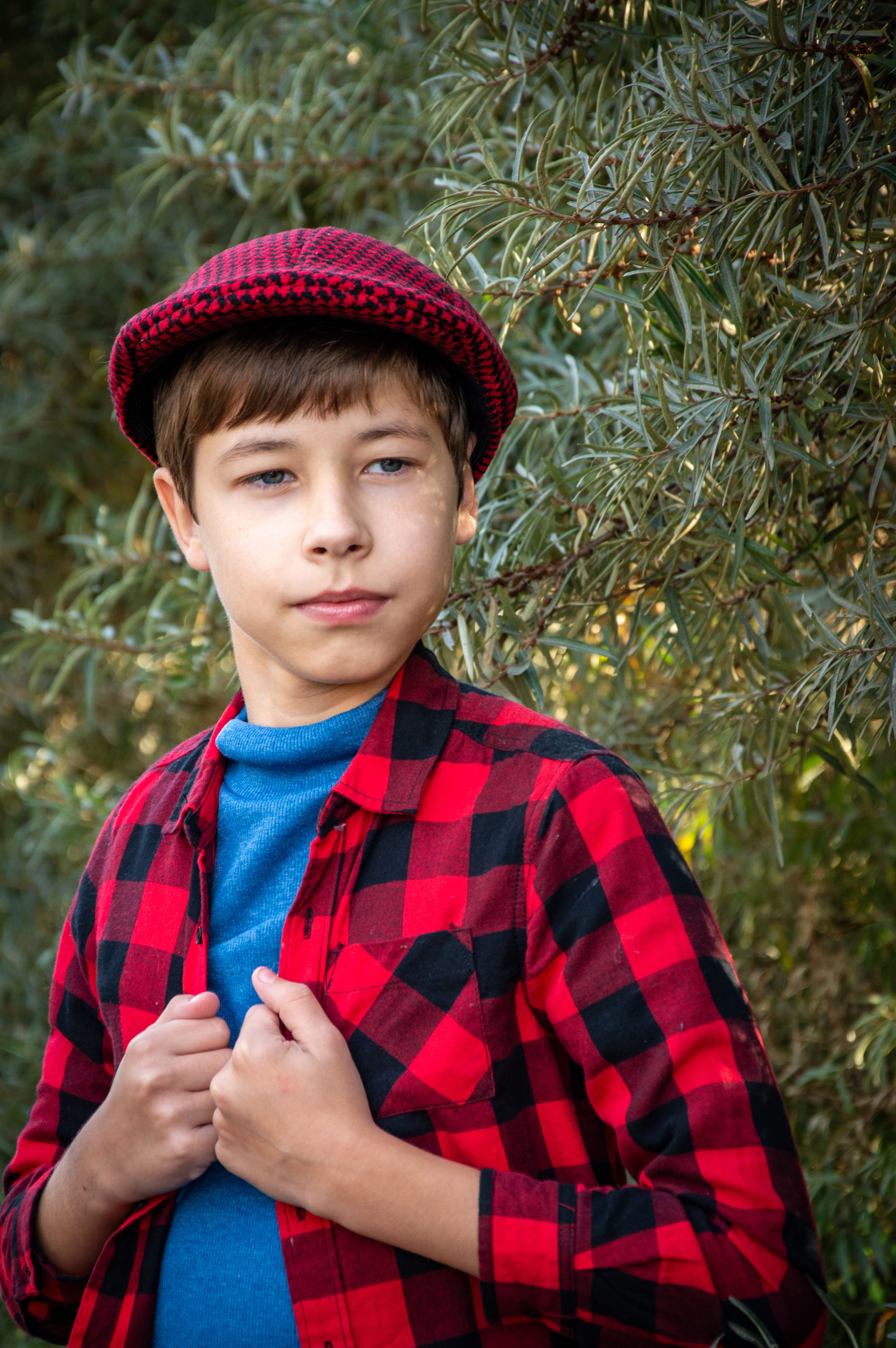 Portrait of a young boy wearing a red plaid shirt and hat, standing outdoors.