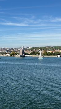 A sailboat gliding past the iconic Belém Tower on a sunny day in Lisbon, Portugal.