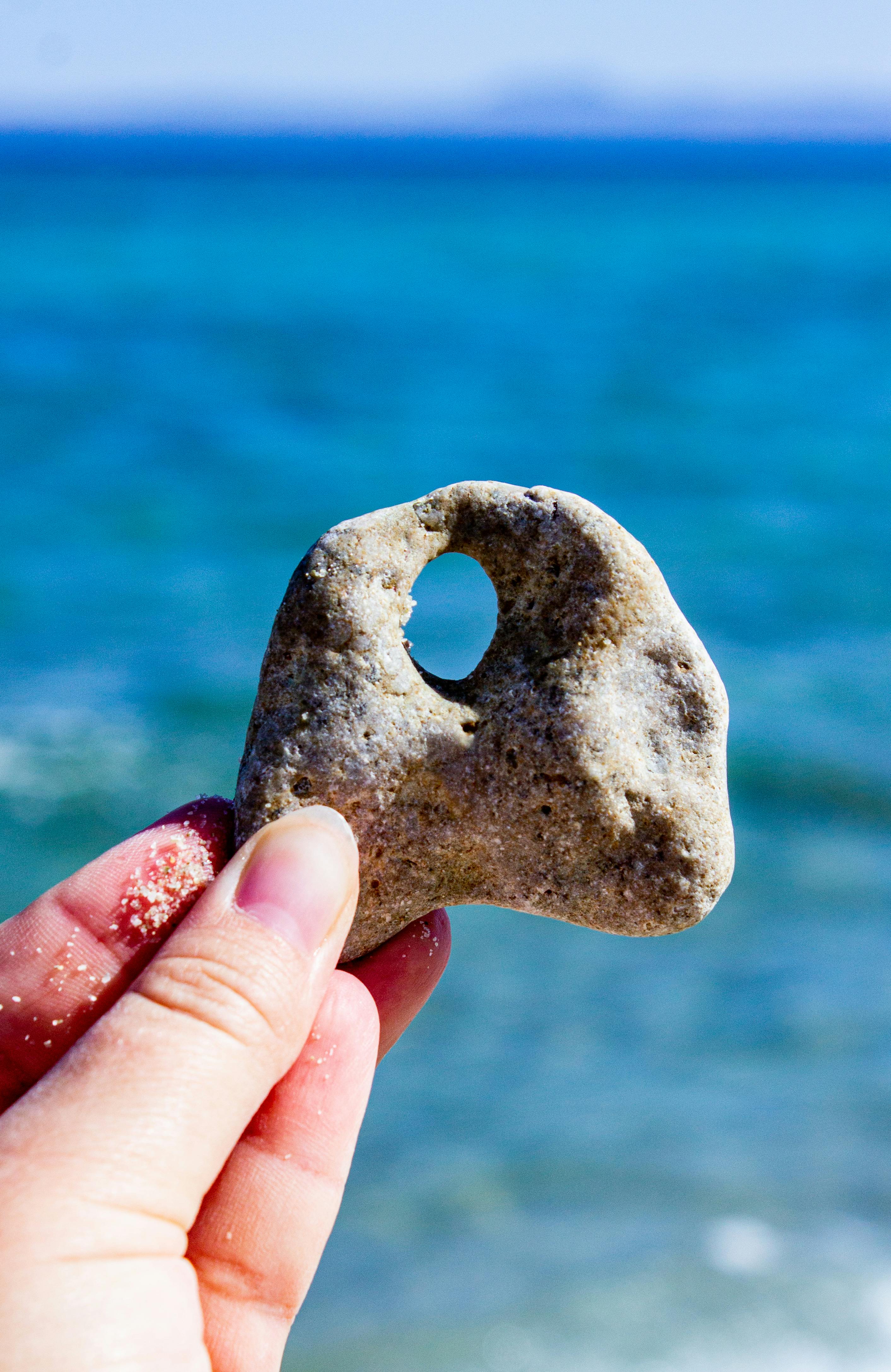 在希腊的蓝色爱琴海中，特写镜头捕捉到了一只手正拿着一个有洞的石头