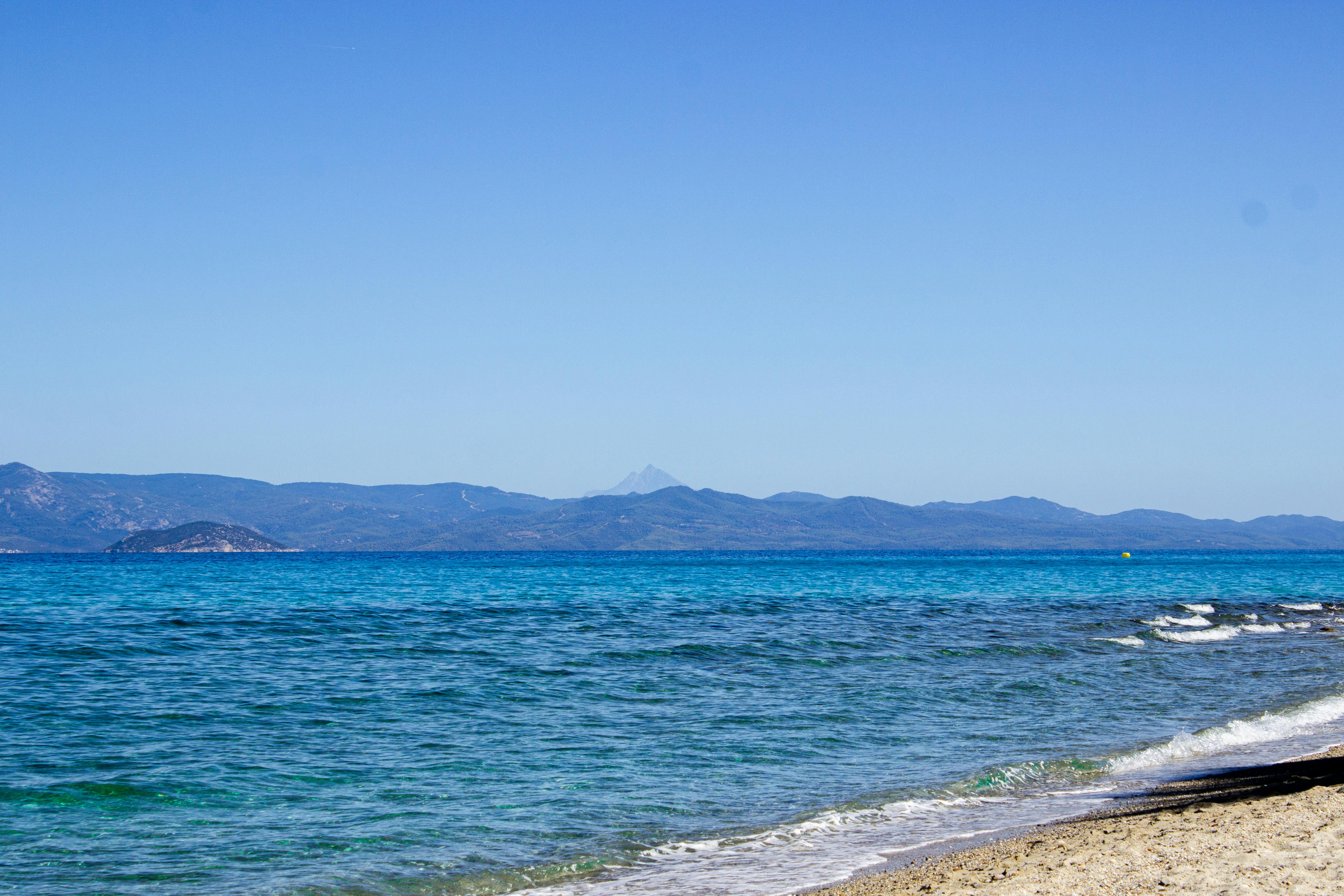 希腊的海滩景观令人惊叹，展示了清澈的蓝色海水和遥远的山脉