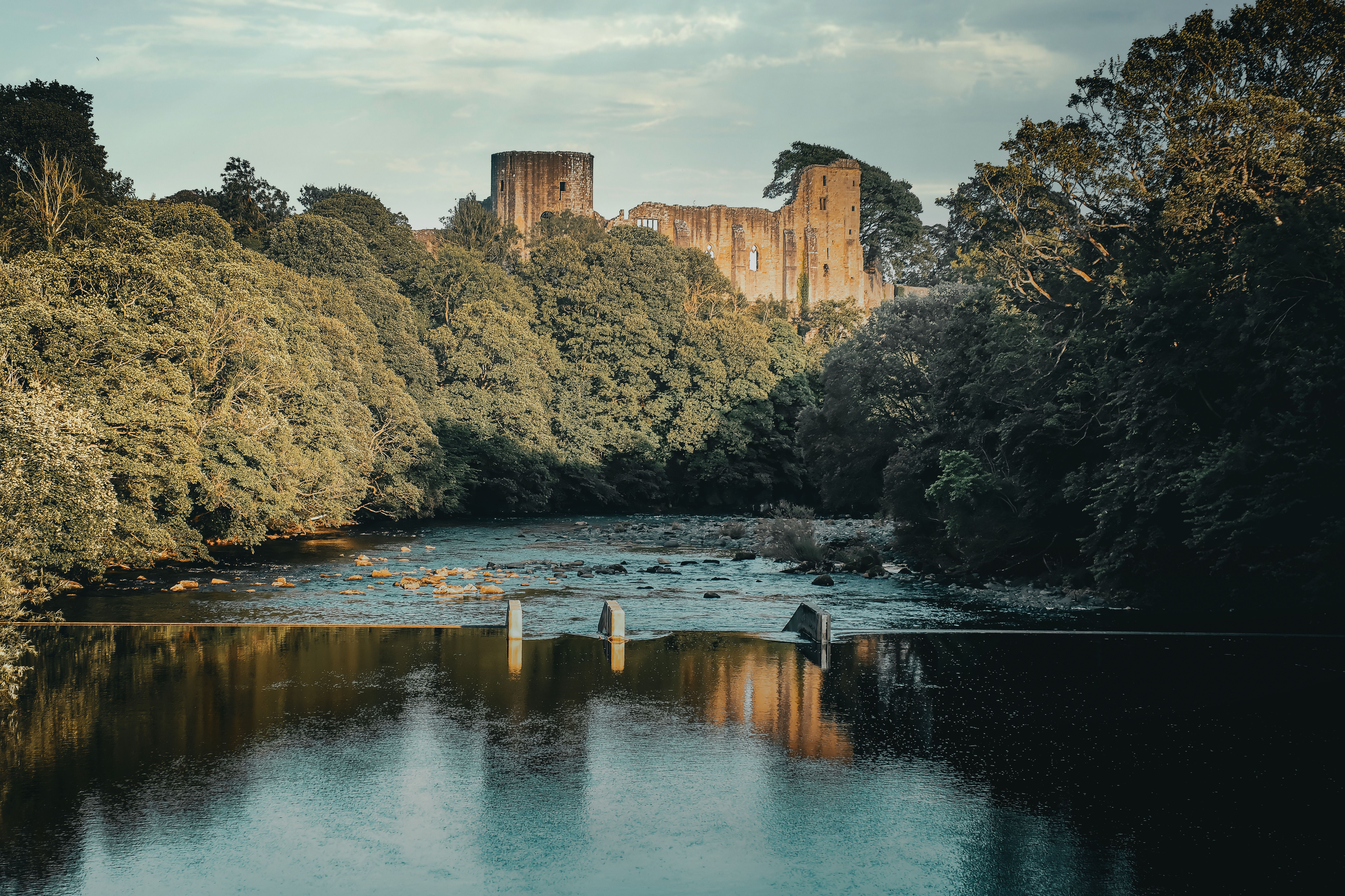 Capture of Barnard Castle ruins set amid a lush, tranquil summer landscape reflecting on a serene river.