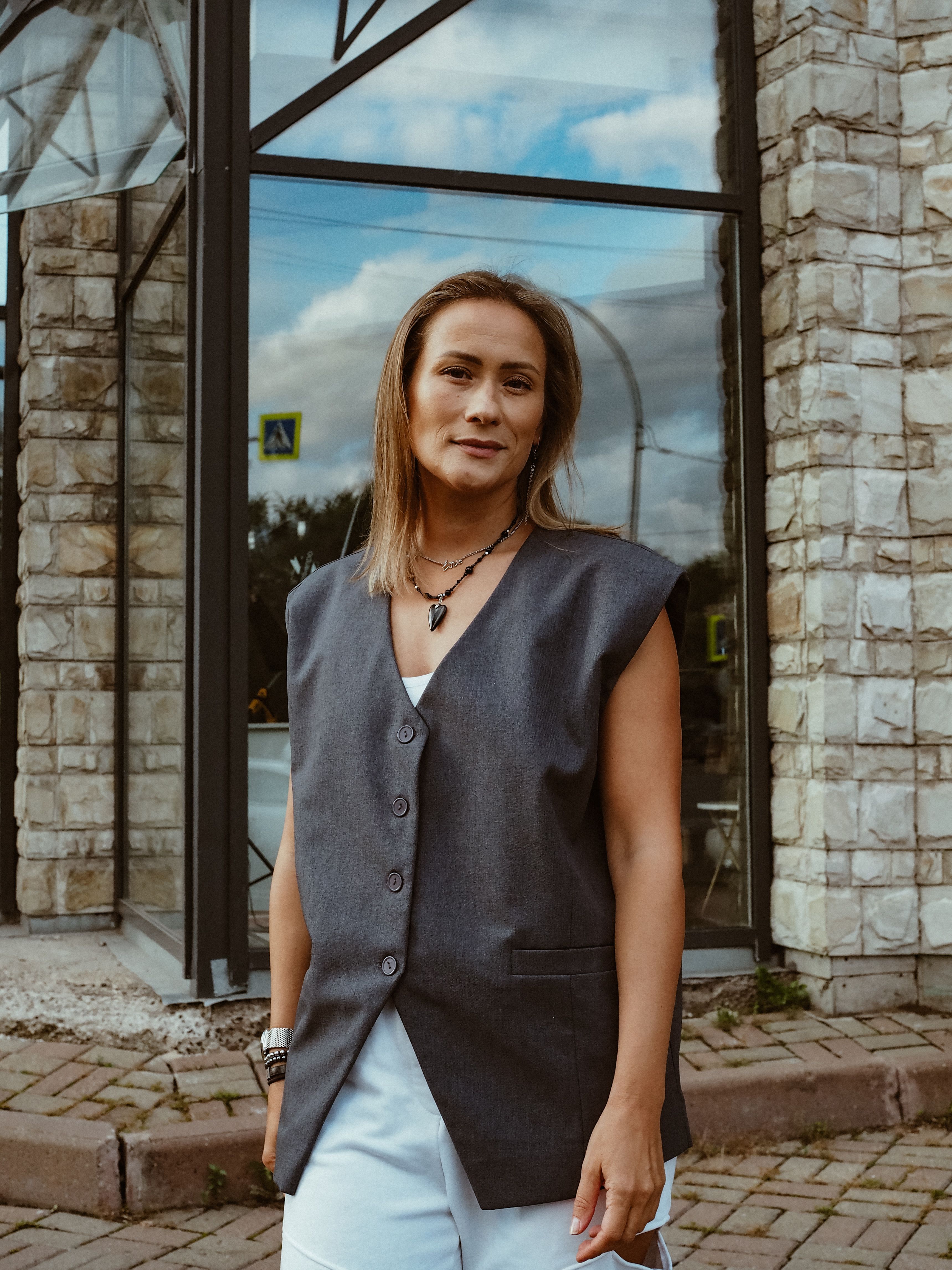 Free Confident woman in a casual vest poses outside a modern building. Stock Photo