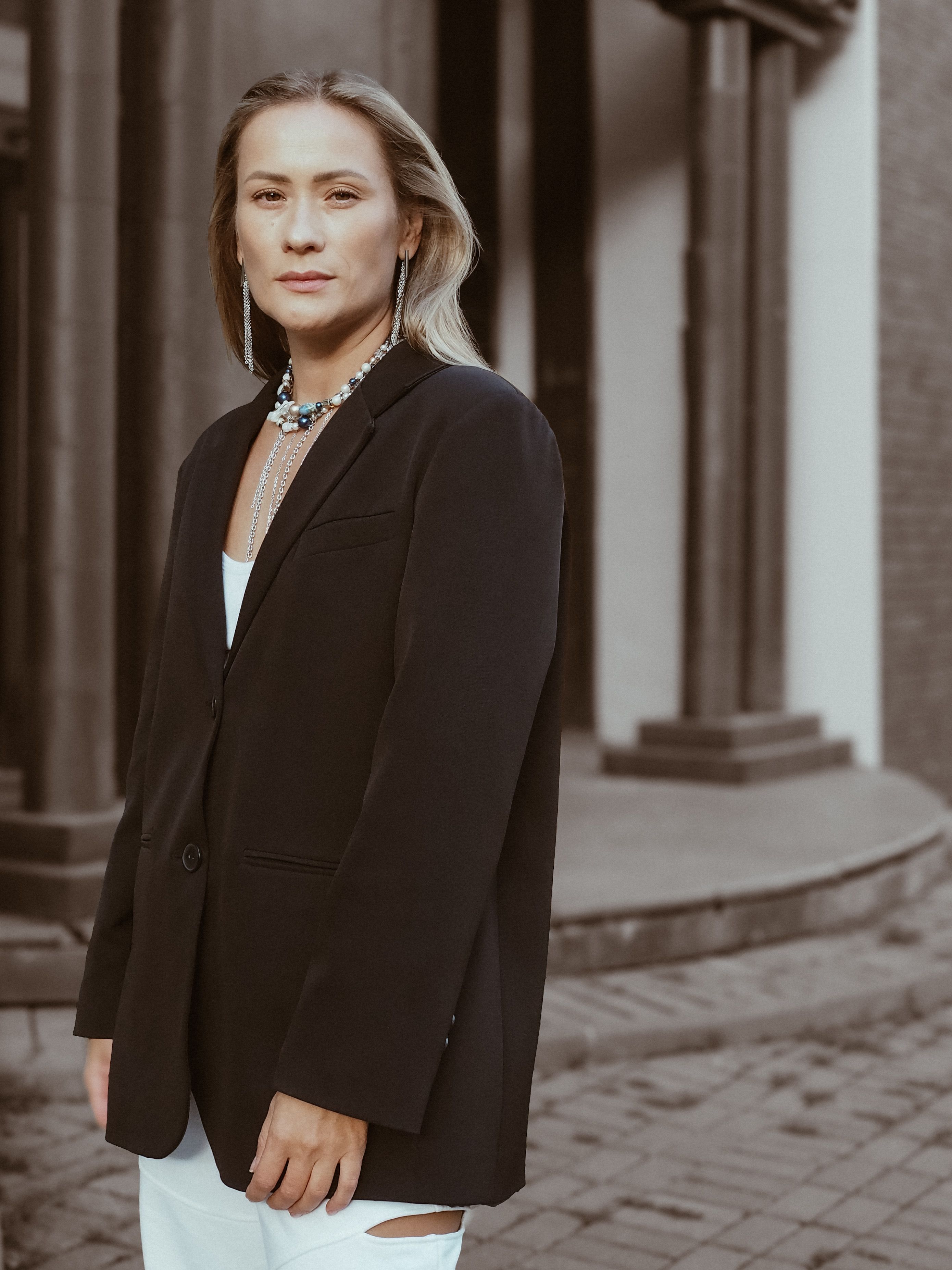 Free Fashion-forward adult in black blazer and jewelry poses outdoors. Stock Photo