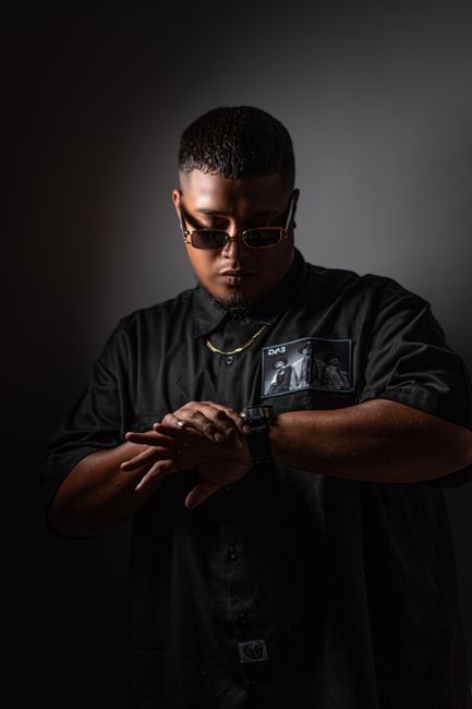 Stylish man wearing sunglasses and jewelry with a focused expression, checking his watch.