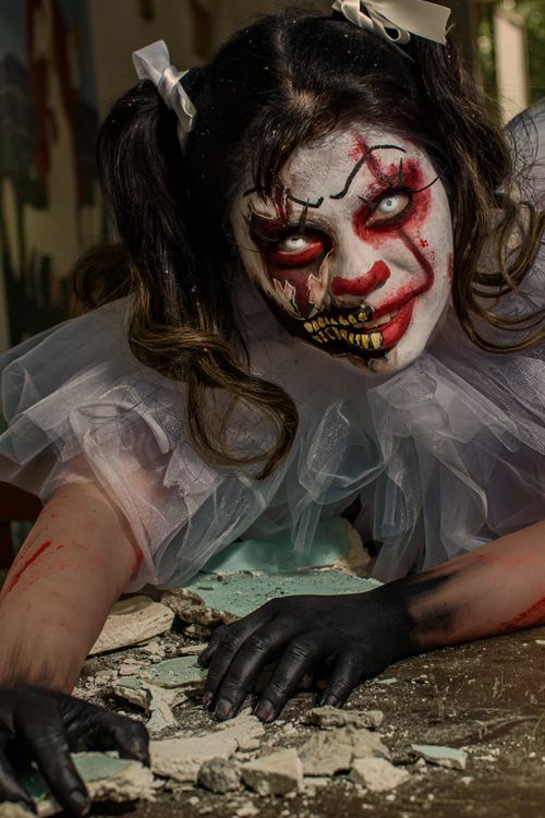 Free Creepy clown with intense makeup crawling on rubble, perfect for horror themes or Halloween imagery. Stock Photo
