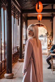 Fashionable woman in elegant attire walking through an Asian-influenced corridor.