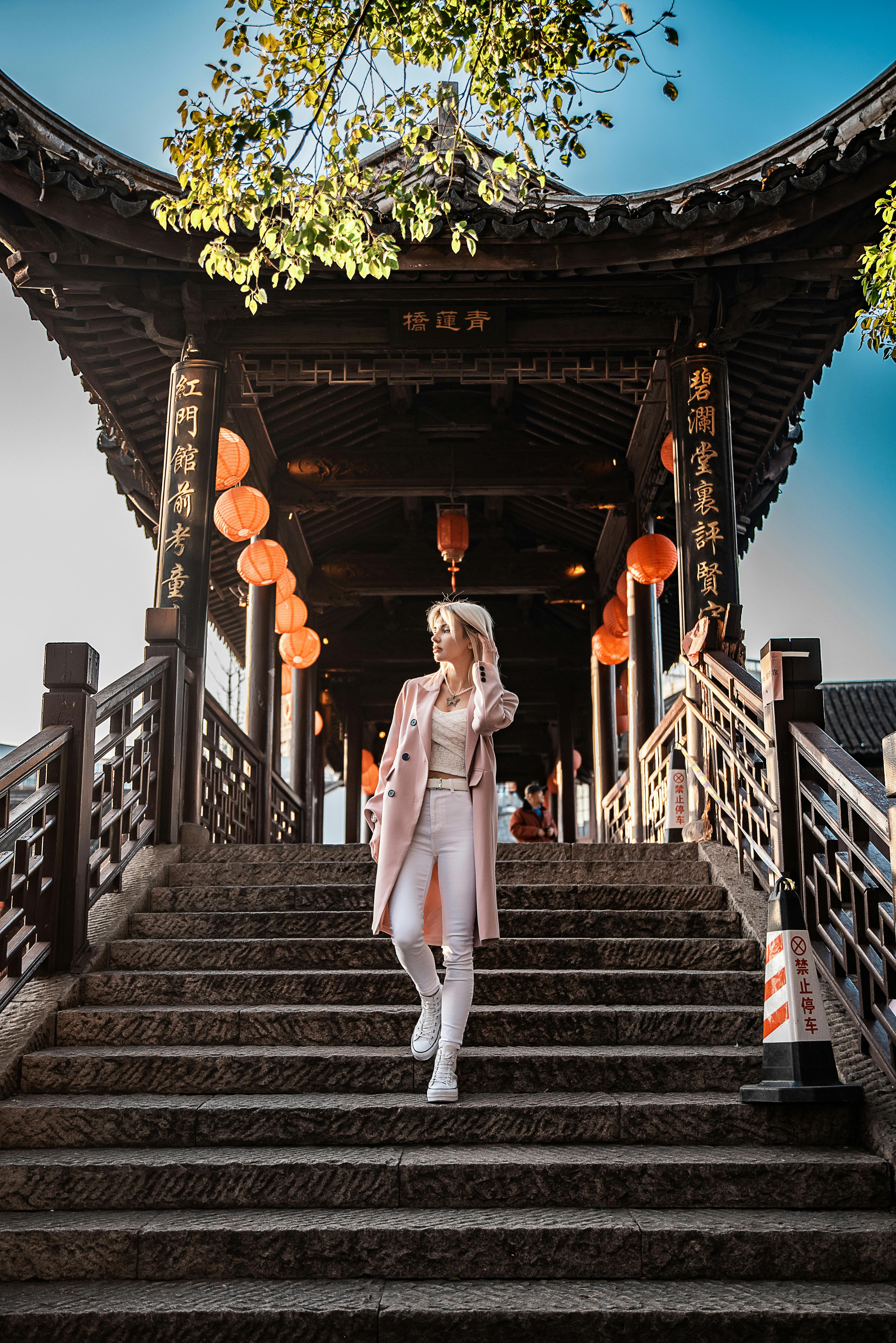 走在一座有充满活力的灯笼装饰的中国桥梁上的，是一位穿着粉红色外套的时髦妇女