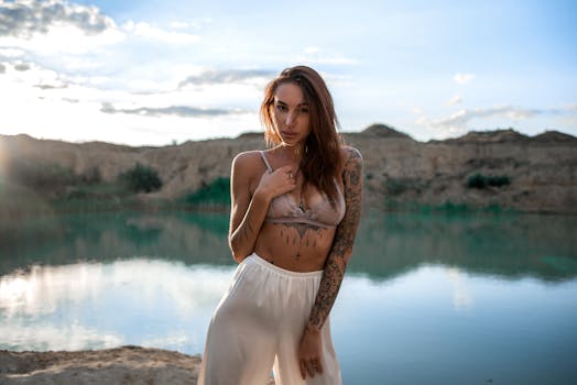 在日落时分，一名女子在湖边摆姿势，纹身增添了她的风采