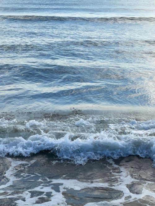 Free Serene ocean waves rolling onto the sandy beach at sunset, creating a tranquil scene. Stock Photo