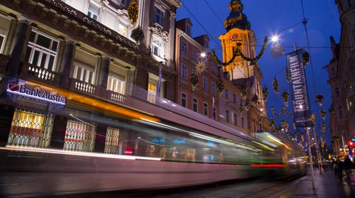 Free Street illuminated by festive lights with a moving tram in Graz, Austria, creating a dynamic night scene. Stock Photo