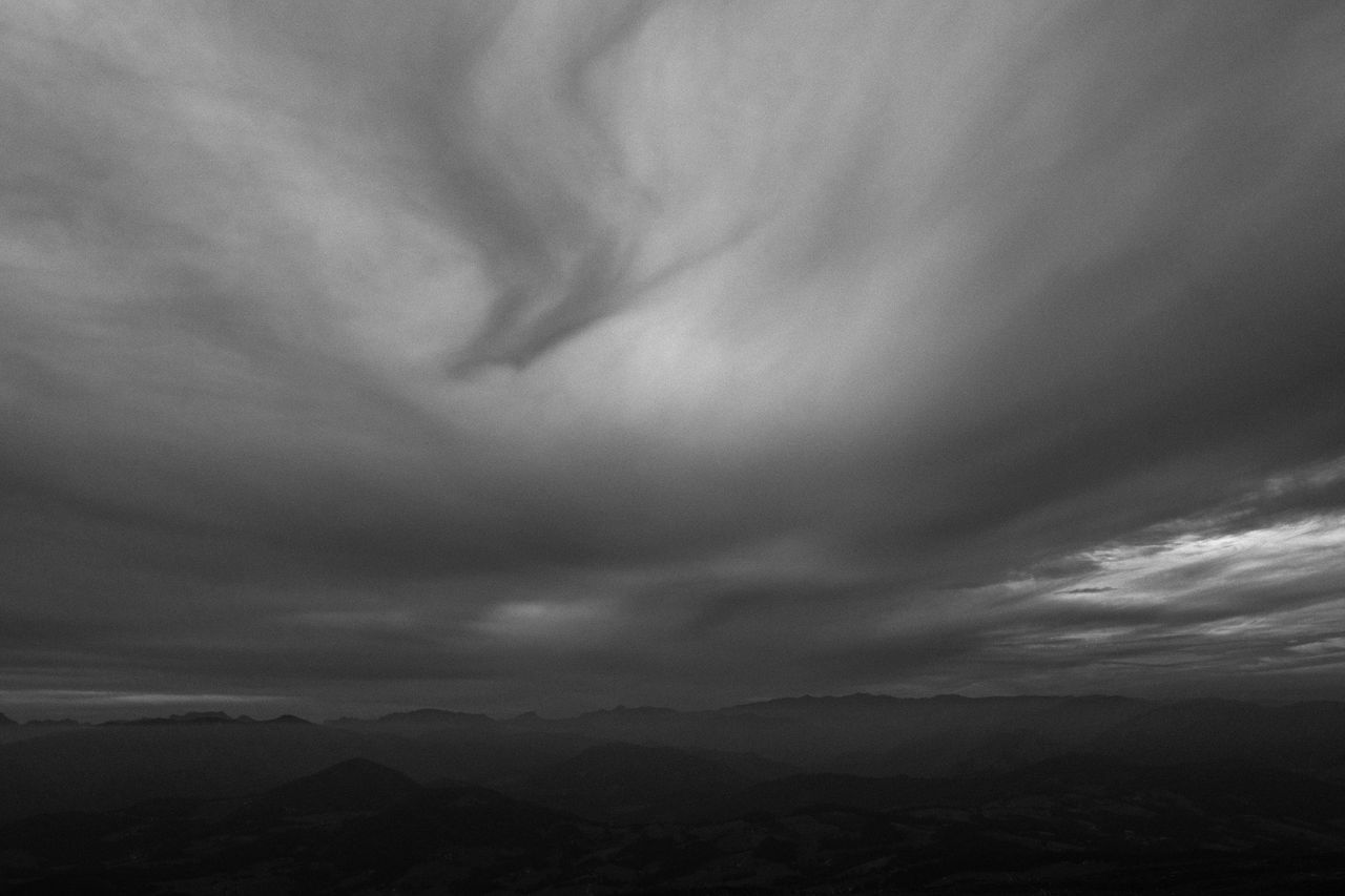 black and white photo of dramatic clouds over a mountain range creatin