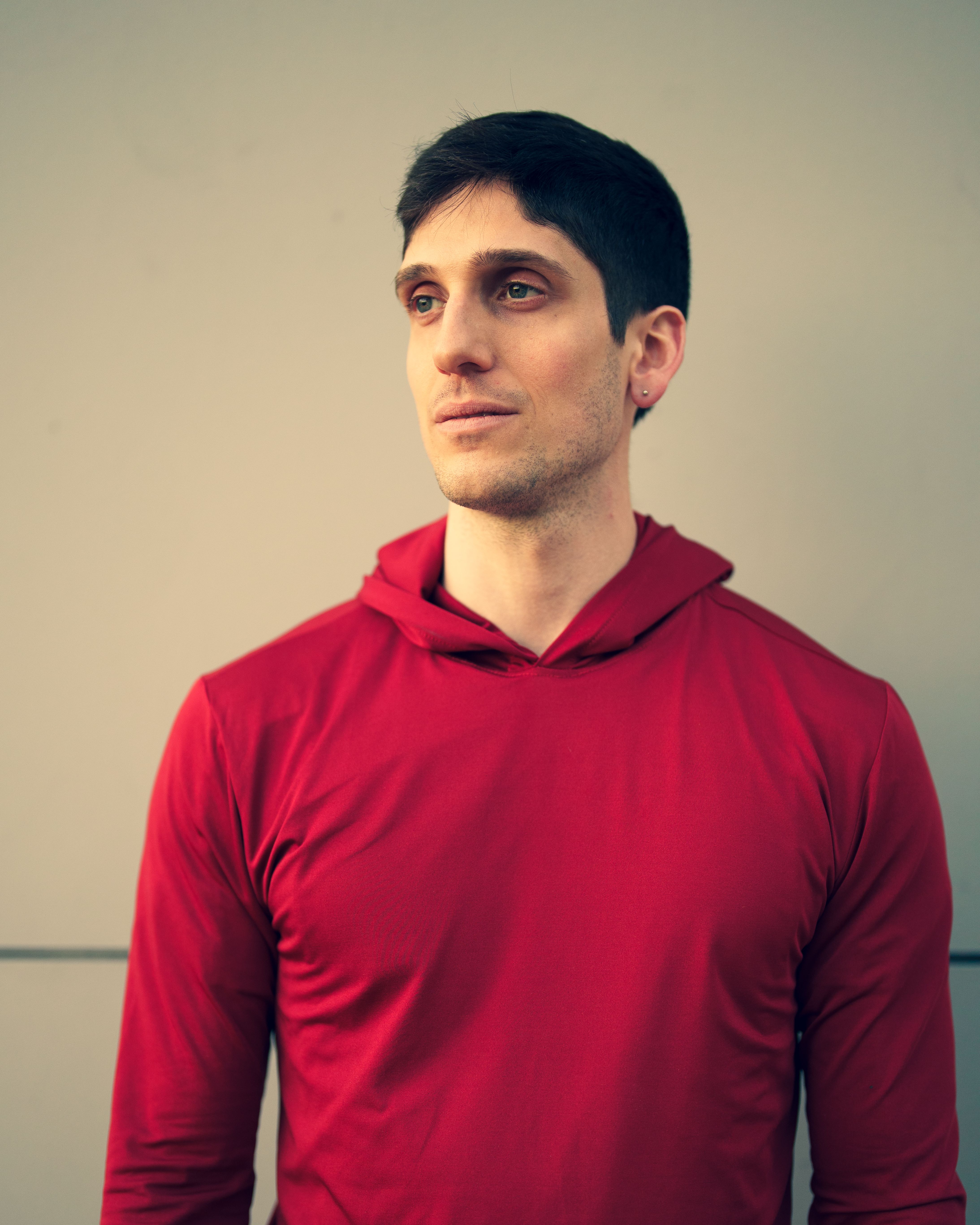 Profile portrait of a young man in a red hoodie against a plain background in Buenos Aires.