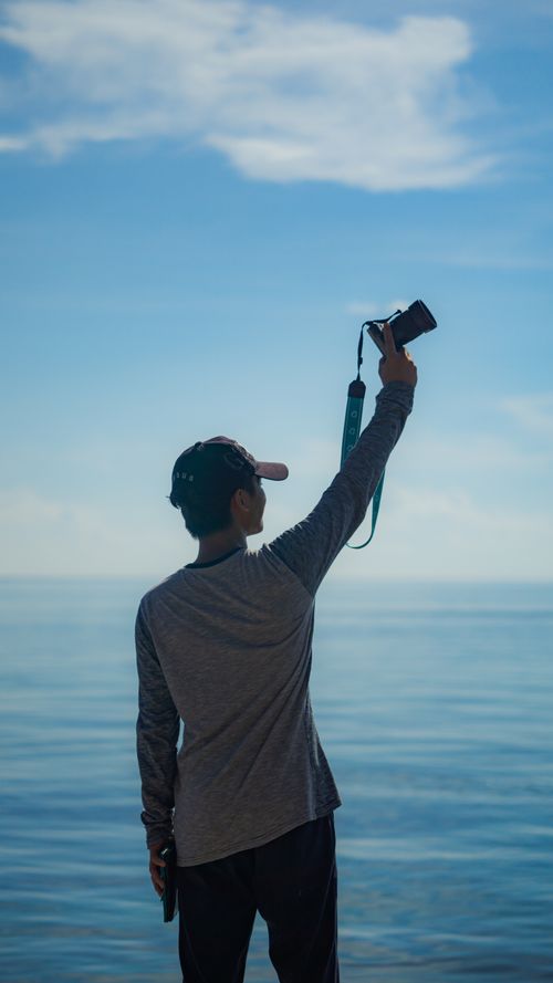 Free A person capturing the ocean view with a camera on a bright, cloud-speckled day. Stock Photo