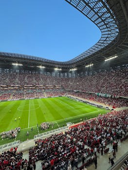 High-energy football match at a packed stadium, showcasing vibrant crowd and architecture.