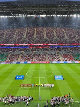 Aerial view of a football match kickoff in a vibrant, full stadium.