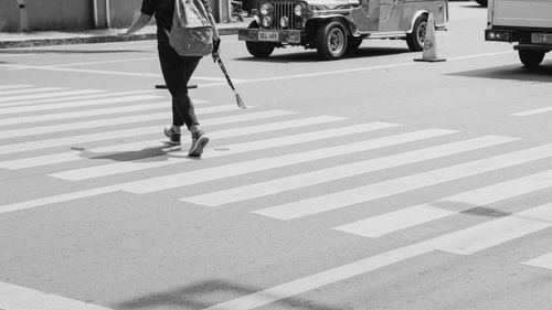 Free A black and white image of a person crossing a zebra crossing with a vintage jeepney in the background. Stock Photo
