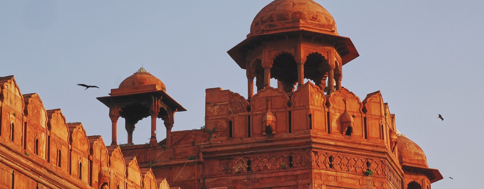 Close-up of Red Fort's intricate architecture at sunset with flying birds.