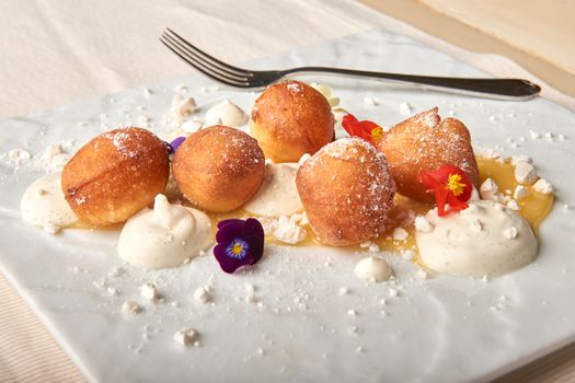 Delicious golden pastry balls dusted with powdered sugar, served with cream and edible flowers.