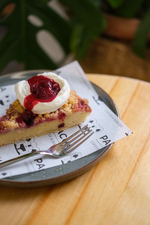 Free A delectable slice of cherry crumble cake topped with cream on a plate in a cozy café. Stock Photo