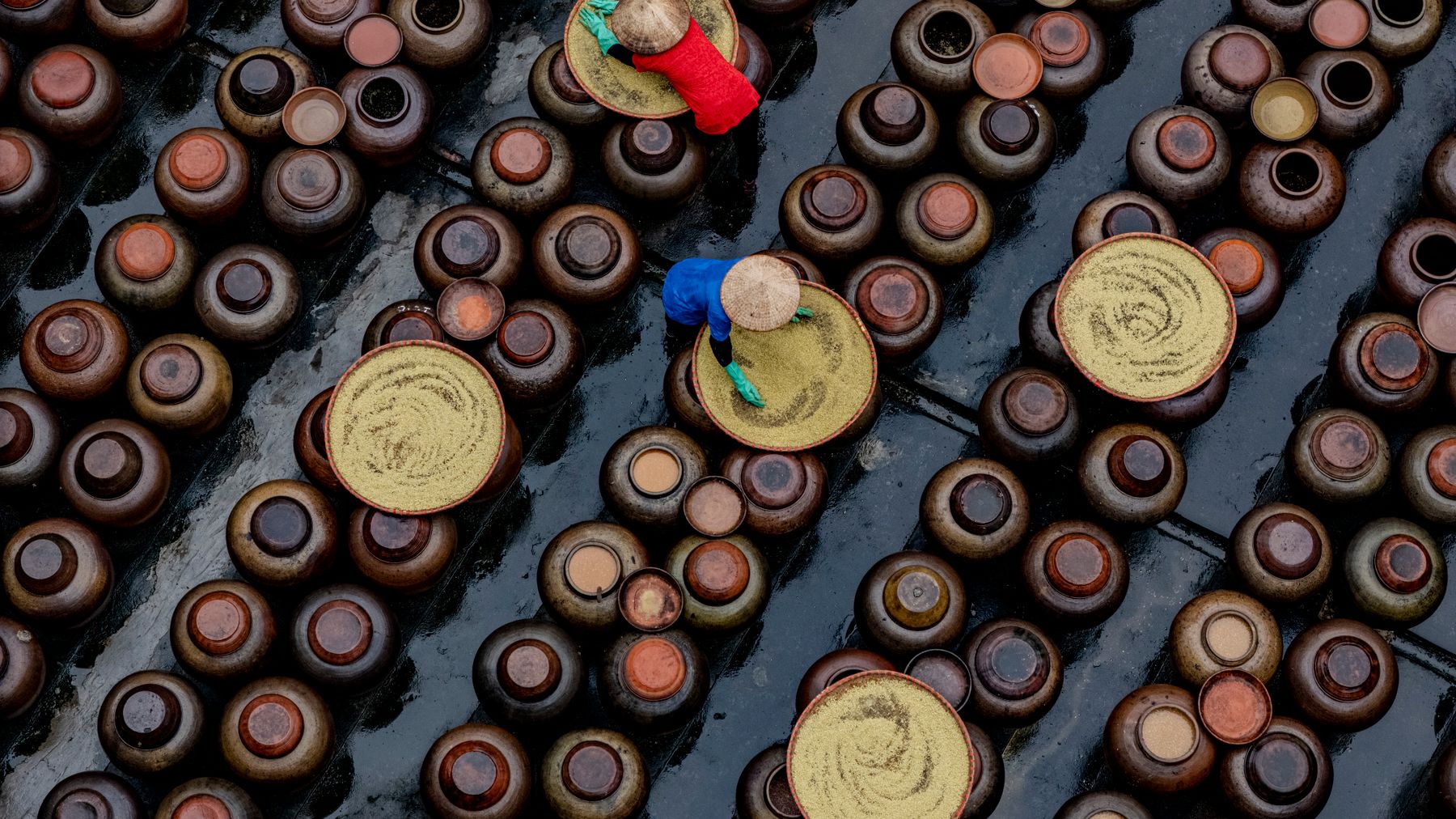 Aerial view of workers in colorful attire preparing soy sauce in ceramic jars in Vietnam.