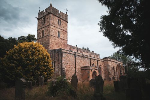Free Gothic-style church with graveyard in Brancepeth, England, surrounded by trees and overcast sky. Stock Photo