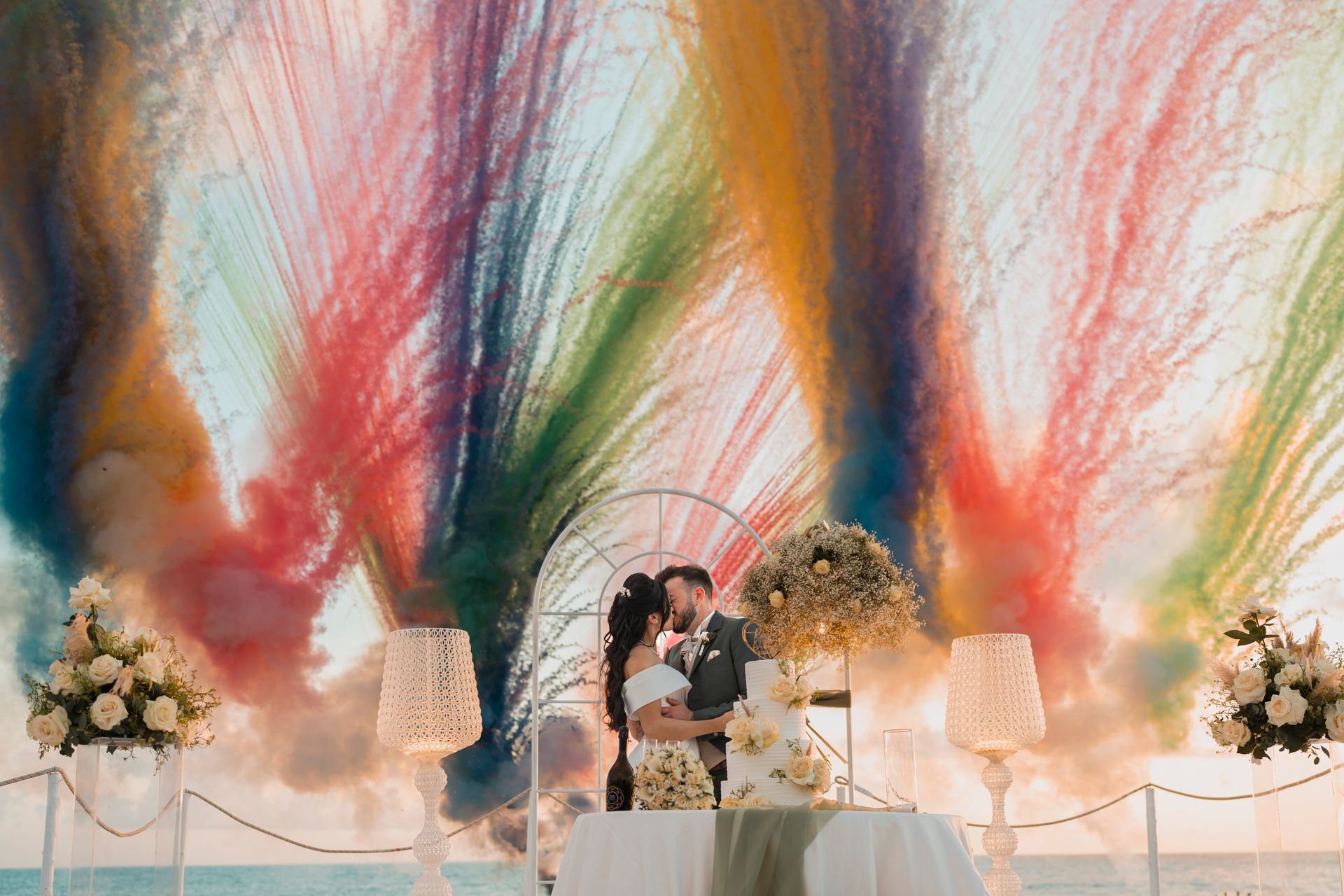 Couple kissing at a wedding with vibrant fireworks and elegant decor.