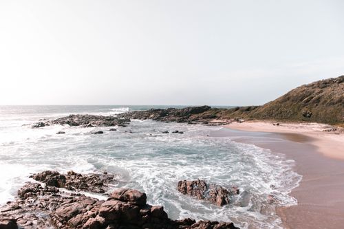 Free Majestic scenery of foamy waves of ocean washing sandy coast surrounded by rocky hills and formations on sunny day Stock Photo