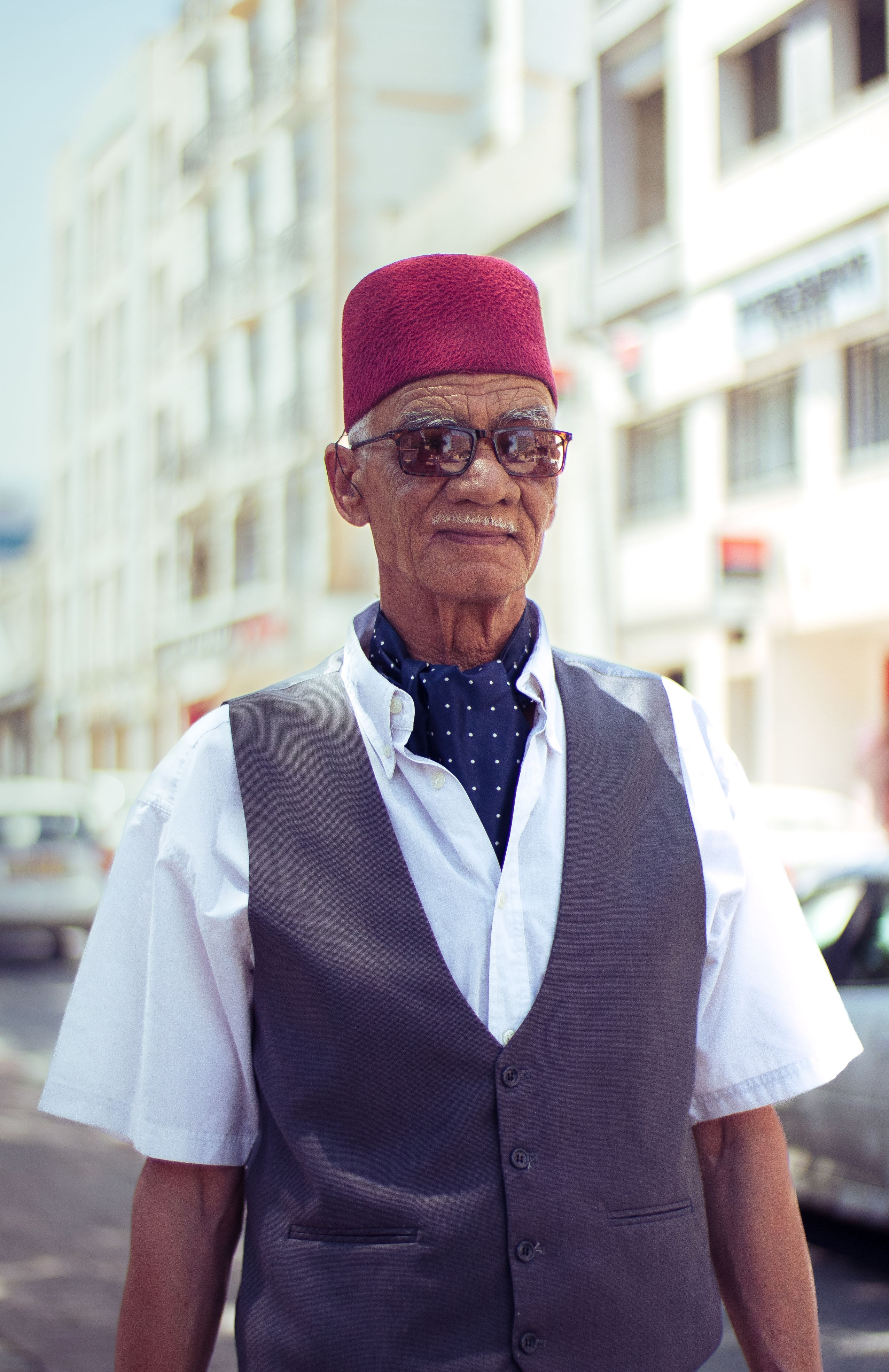 Portrait of a senior man wearing a fez, captured on a sunny day in the city.