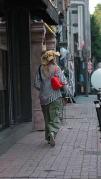 A stylish woman strolls down a quaint street in Istanbul, carrying a vibrant red bag.