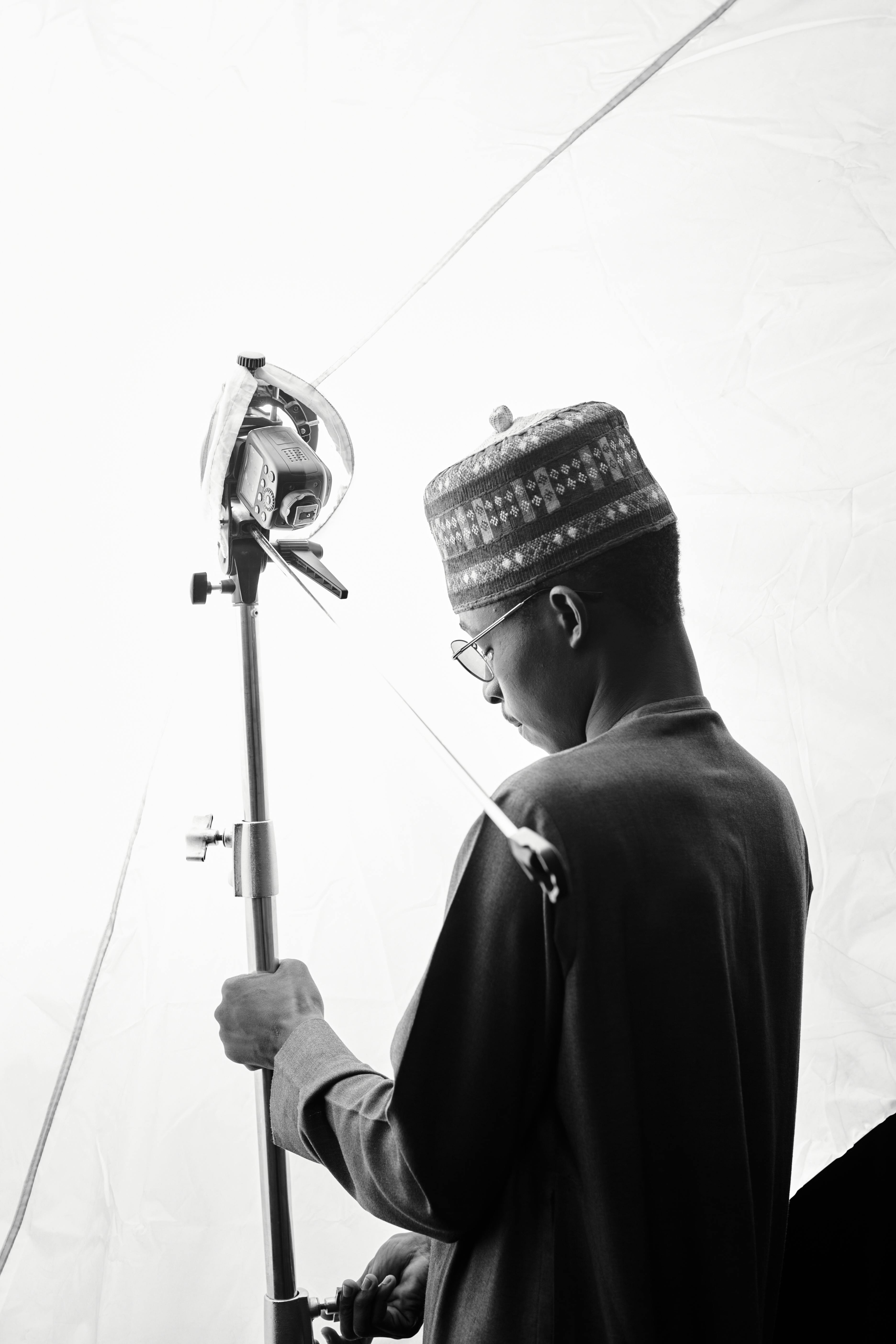 Free Black and white photo of a man in traditional attire adjusting studio lighting. Stock Photo