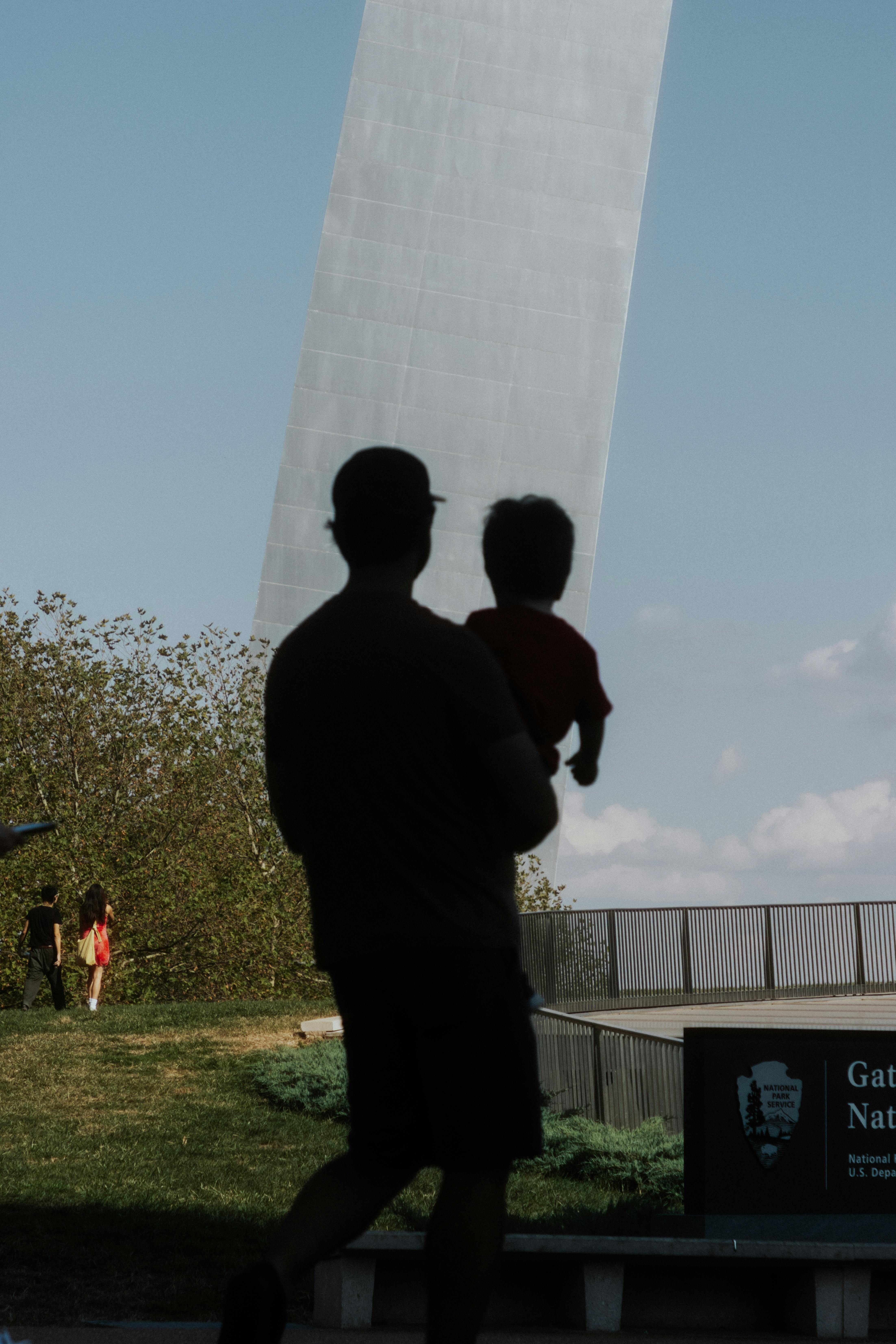Silhouette of a father holding child near Gateway Arch with blue sky.