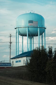 A large blue water tower with an American flag in a rural landscape.