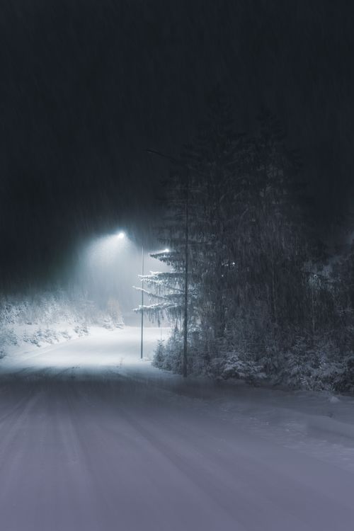 Free Calm winter night scene of a snow-covered road illuminated by streetlights, creating a peaceful atmosphere. Stock Photo