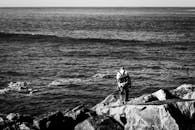 黑白照片中，一个人站在海边的岩石上，显得平静而内省