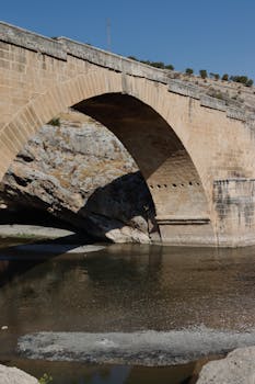 古老的石拱桥在清澈的蓝天下倒映着宁静的河流