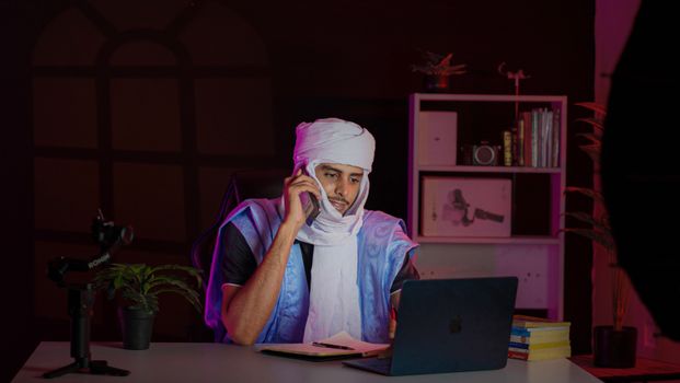 Middle Eastern man in traditional attire working on laptop at night.